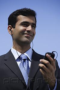 PictureIndia - Indian businessman listening to music outside.