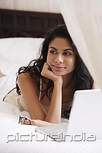 PictureIndia - Indian woman laying on bed smiling with laptop