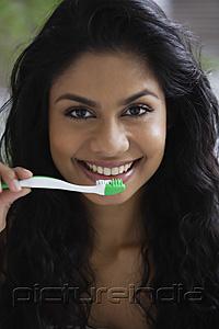 PictureIndia - Head shot of Indian woman brushing her teeth and smiling.