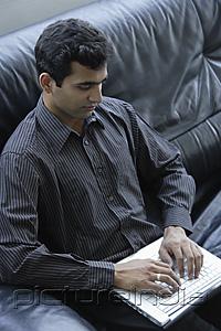 PictureIndia - Indian businessman sitting on black sofa with laptop.