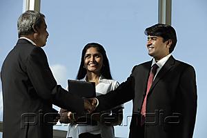 PictureIndia - Business men shaking hands while female colleague looks on.