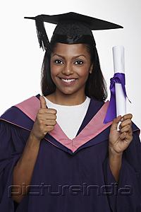PictureIndia - Young woman wearing cap and gown and holding diploma giving thumbs up sign