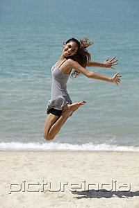 PictureIndia - happy young woman jumping in air at the beach