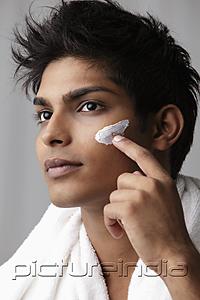 PictureIndia - head shot of young man putting lotion on his face