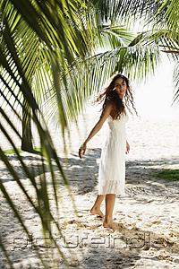 PictureIndia - young woman walking on beach with coconut trees in background