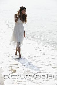 PictureIndia - young woman wearing a white dress walking along the beach