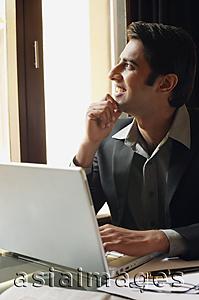 Asia Images Group - business man working at laptop, hand on chin, looking out window