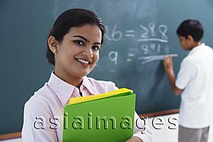 Asia Images Group - smiling teacher holding notebooks, boy at chalkboard