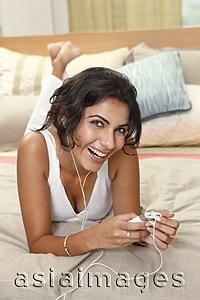 Asia Images Group - Young woman listening to music on bed