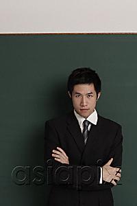 AsiaPix - Businessman standing against black wall with arms crossed