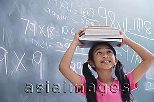 Asia Images Group - girl with books stacked on head, looking up (horizontal)