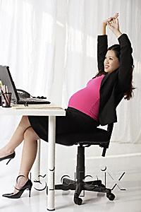 AsiaPix - Profile of pregnant businesswoman at desk stretching