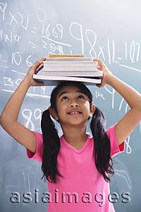 Asia Images Group - girl with books stacked on head, looking up (vertical)