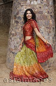 Asia Images Group - young woman in sari walking, stone pillar