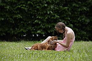 Mind Body Soul - Young woman sitting on grass, holding her dog's face in hands