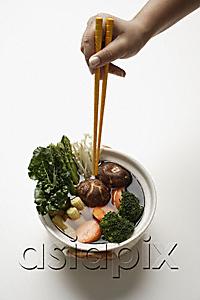AsiaPix - hand holding chopsticks in clay pot of vegetables