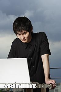 Asia Images Group - young man standing, using laptop