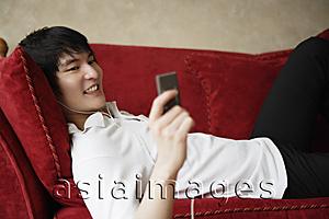 Asia Images Group - young man laying on sofa, MP3 player