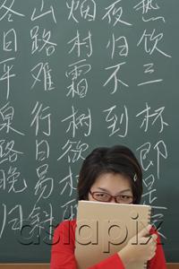 AsiaPix - student hiding behind notepad in front of chinese characters written on chalk board