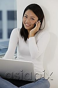 AsiaPix - Young Asian woman talking on phone while looking at laptop