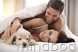Mind Body Soul - Young couple playing with puppy in bed