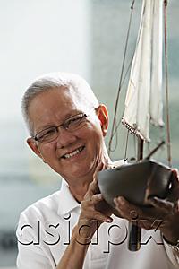 AsiaPix - head shot of mature man holding model sail boat and smiling