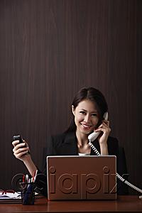 AsiaPix - Young woman sitting at her desk holding her phones