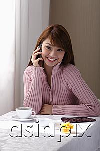 AsiaPix - Young woman sitting at table with coffee and talking on phone