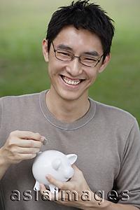 Asia Images Group - Man putting coin into piggy bank