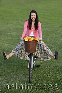 Asia Images Group - Young woman riding bike with legs kicked out