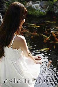 Asia Images Group - Young woman in white dress sitting by pond