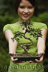 Asia Images Group - Young woman holding up bonsai tree