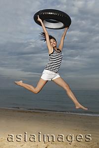 Asia Images Group - Young woman jumping on beach, holding up inner tube