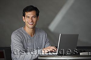 Asia Images Group - man working on laptop, smiling at camera