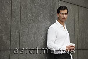Asia Images Group - man in white shirt holding a cup of coffee, leaning against wall