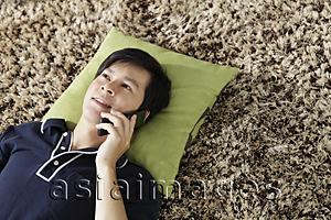 Asia Images Group - Young man lying on floor talking on phone