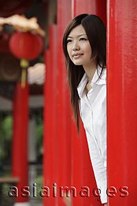 Asia Images Group - Young woman looking out from behind red pillars