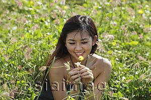 Asia Images Group - young woman looking at flower in grassy field