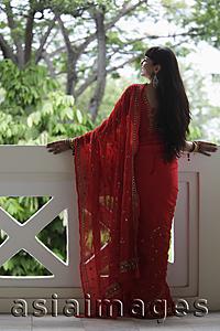 Asia Images Group - Back shot of Indian woman wearing a red sari looking over balcony.