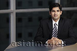 Asia Images Group - Young man sitting at table hands folded