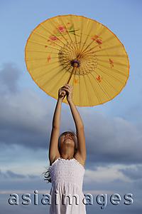 Asia Images Group - young girl holding up yellow Chinese umbrella, bluebsky background
