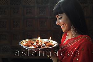 Asia Images Group - Profile shot of Indian woman holding a tray of lit oil lamps