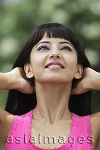 Asia Images Group - Head shot of young Indian woman looking up with hands in her hair.