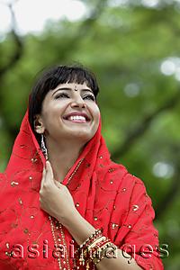 Asia Images Group - Indian woman looking up and smiling with red sari over her head.