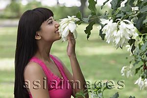 Asia Images Group - profile of young woman smelling flowers outside