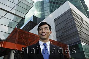 Asia Images Group - Young businessman smiling in front of modern buildings