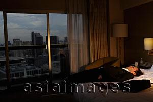 Asia Images Group - man wearing suit and laying down on bed in hotel room in the evening.