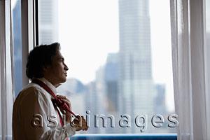 Asia Images Group - Man looking out of window and tying his tie.