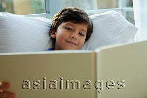 Asia Images Group - Young boy reading book by window and smiling