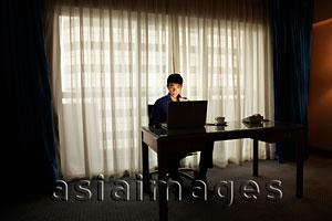 Asia Images Group - Young man sitting at desk working on laptop in the dark